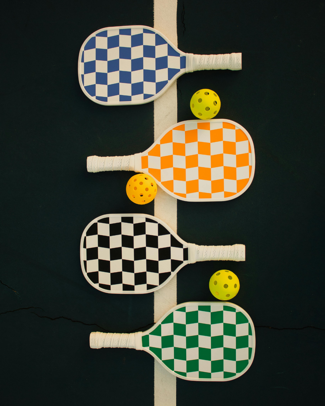 picture of four pickleball ball paddles in a row with pickleballs laying beside them